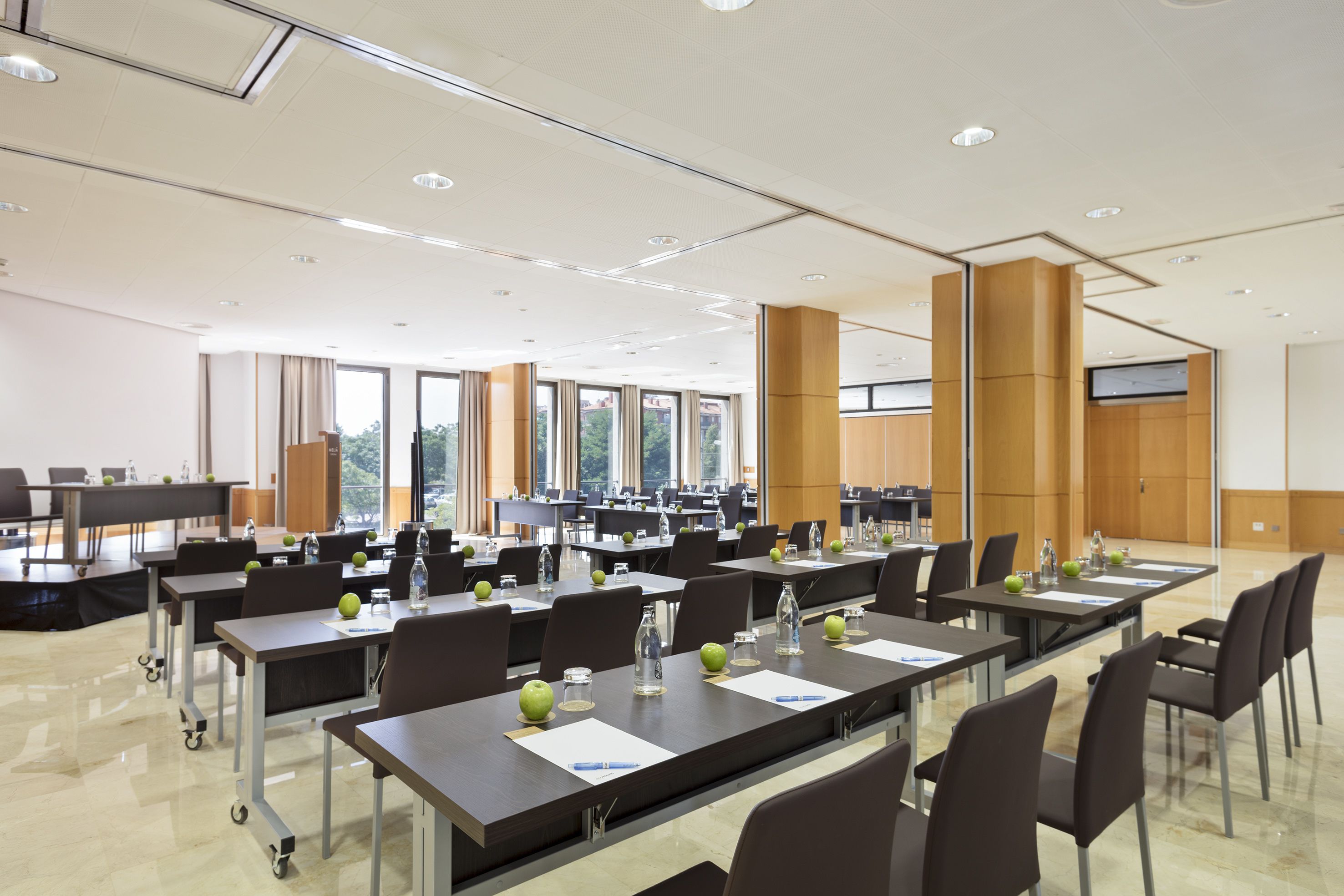 A conference room with multiple tables, chairs, and a large screen.