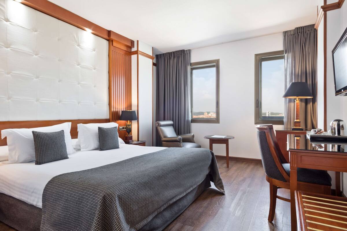 A hotel room with a large bed, a desk with a chair, a TV, and a window with curtains.
