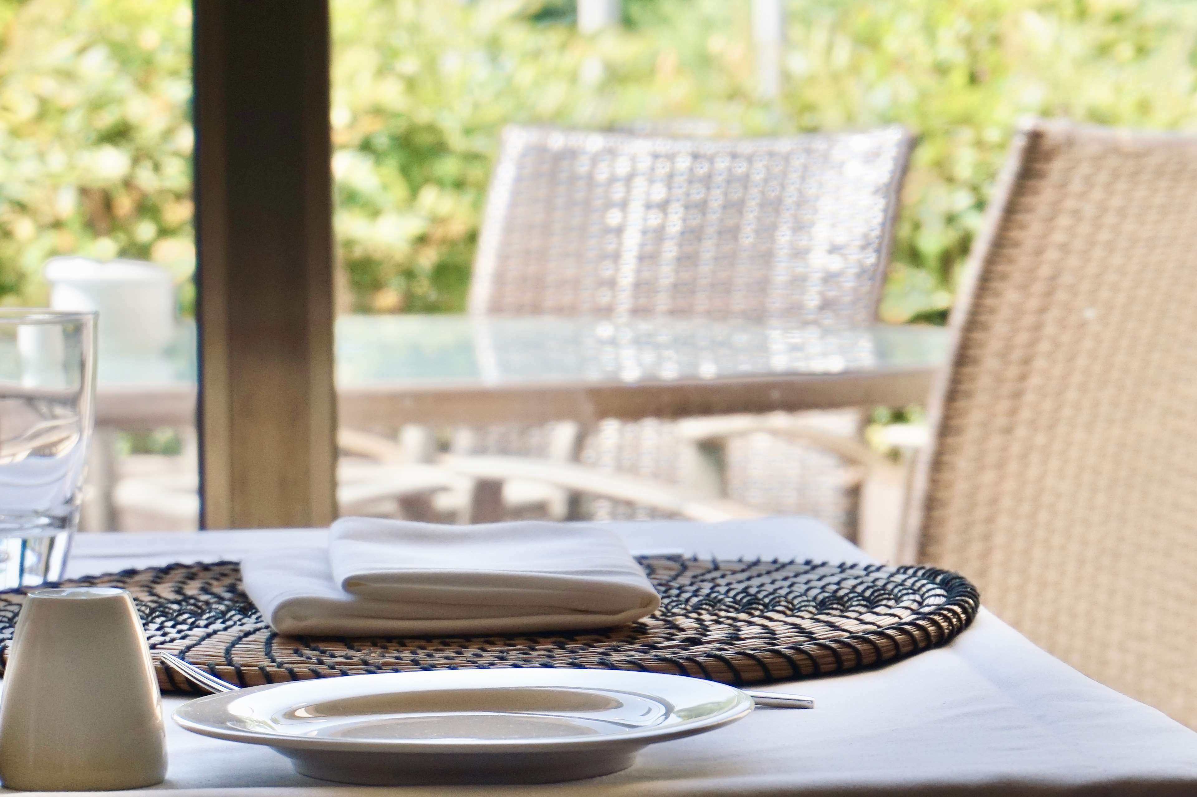 Una mesa dispuesta para comer, con un protector de tela tejido, servilletas dobladas y un vaso de agua.