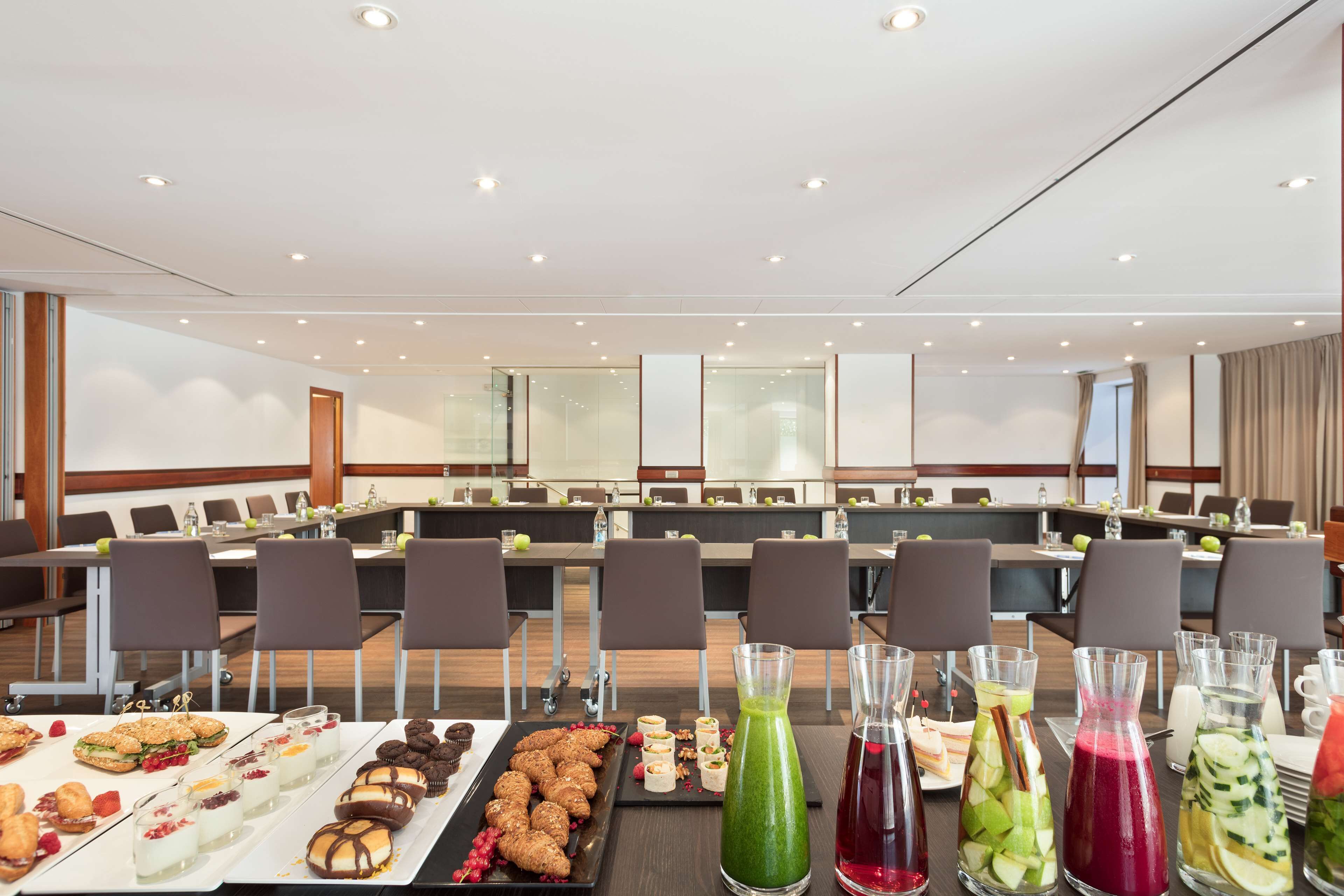 Un salón de conferencias con una larga mesa dispuesta para un bufé, que ofrece diversos aperitivos y bebidas.