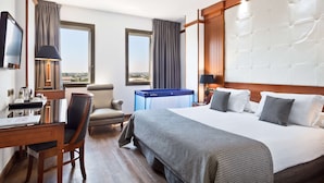 A hotel room with a large bed, a desk with a chair, a television, and a view of the city through the windows. - Best Western Premier CMC Girona (Girona)