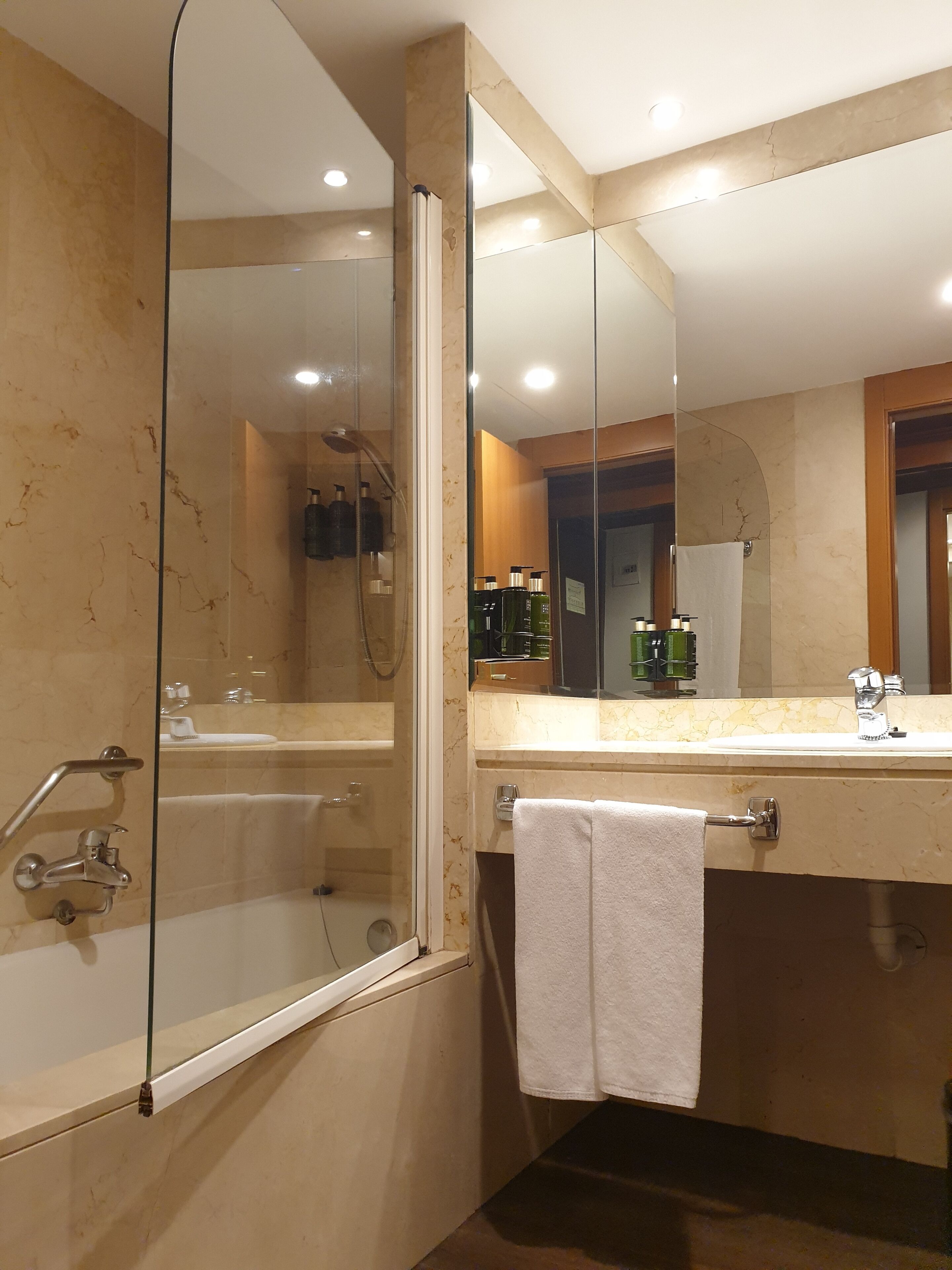 A modern bathroom with a glass-enclosed shower, a vanity with a mirror, and a towel hanging on the door.