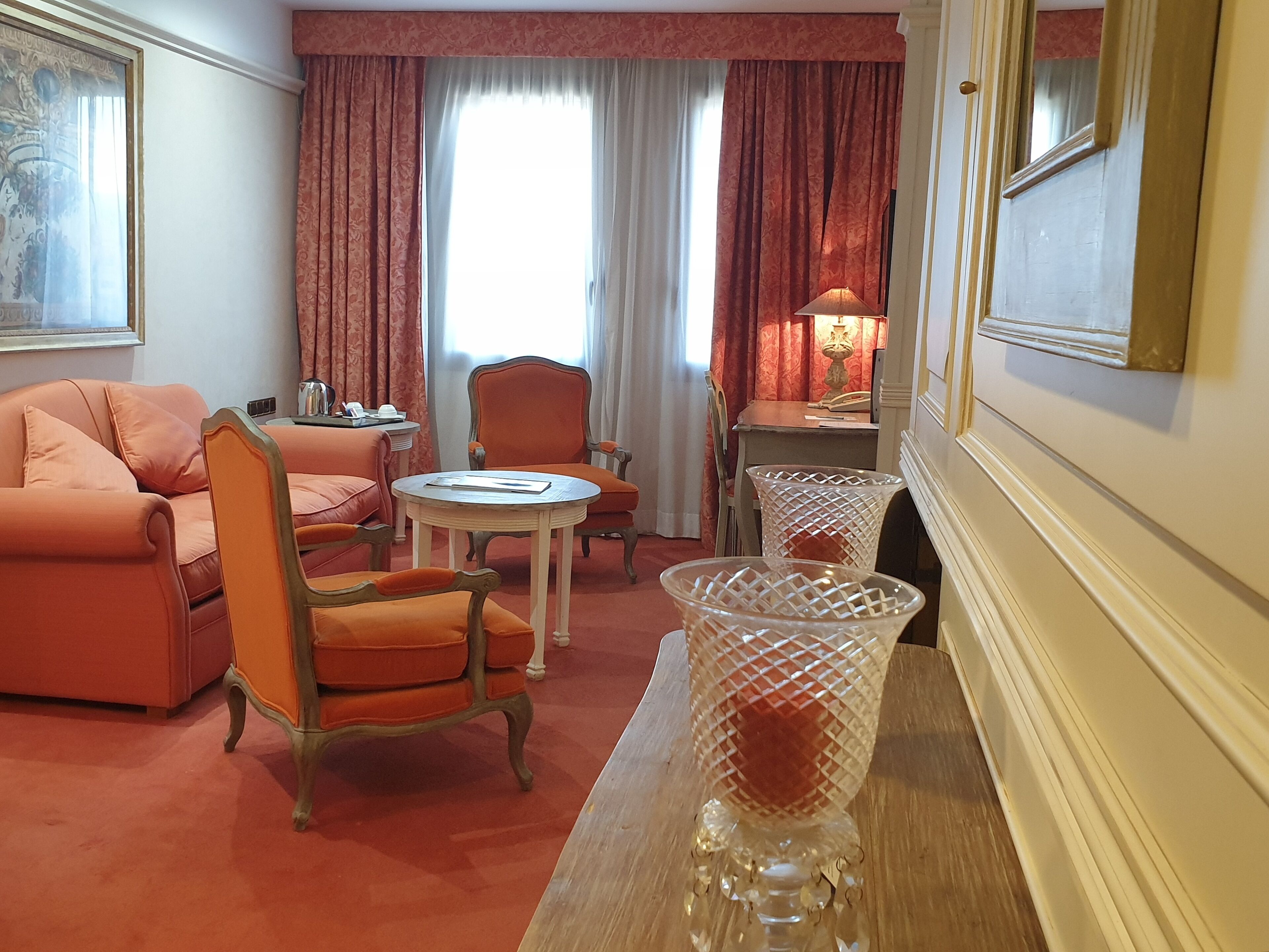 A room with a sofa, chairs, a small table, a lamp, and a decorative vase.