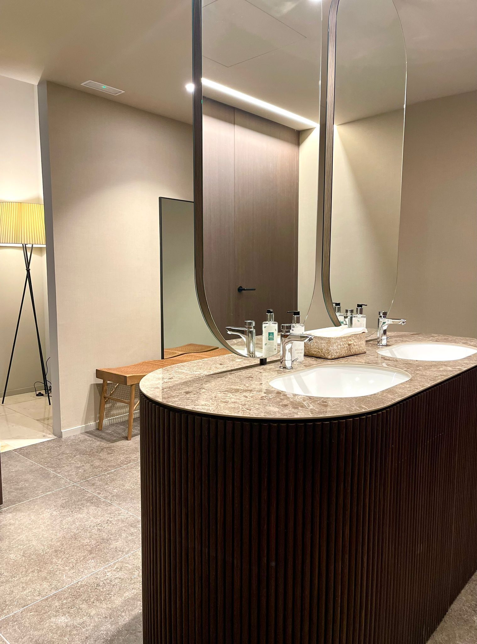 Un baño moderno con tocador curvo, dos lavamanos y un espejo grande.