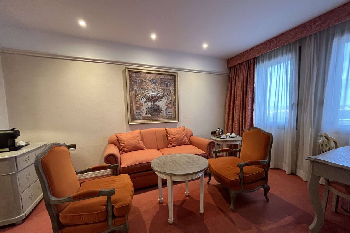 A hotel room with a sofa, two armchairs, a small round table, and a desk.