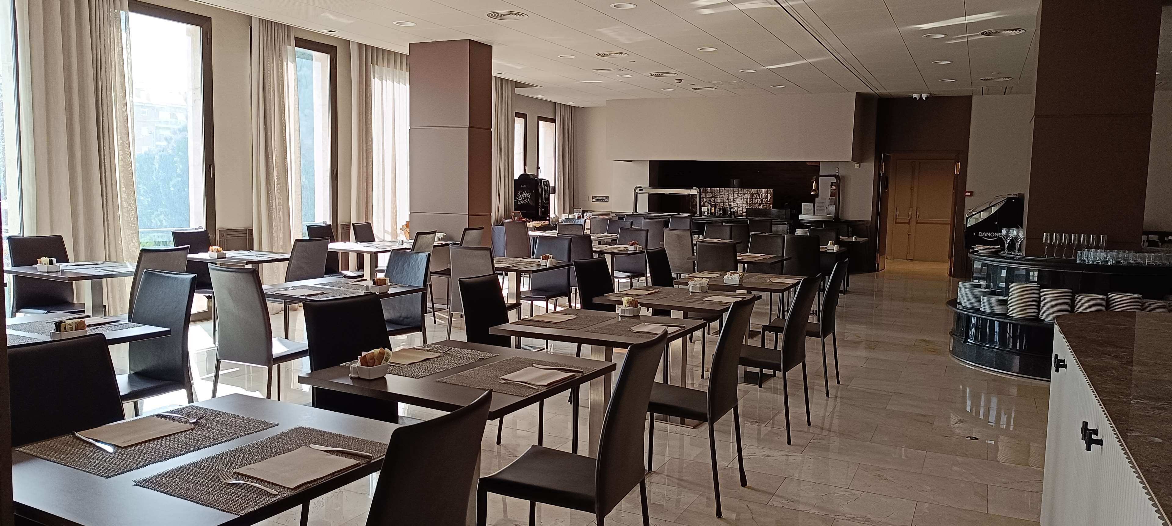 A spacious dining area with multiple tables and chairs, a bar counter, and a large window providing natural light.
