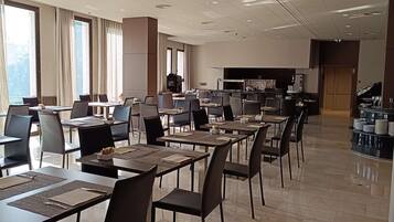 A spacious dining area with multiple tables and chairs, a bar counter, and a large window providing natural light.