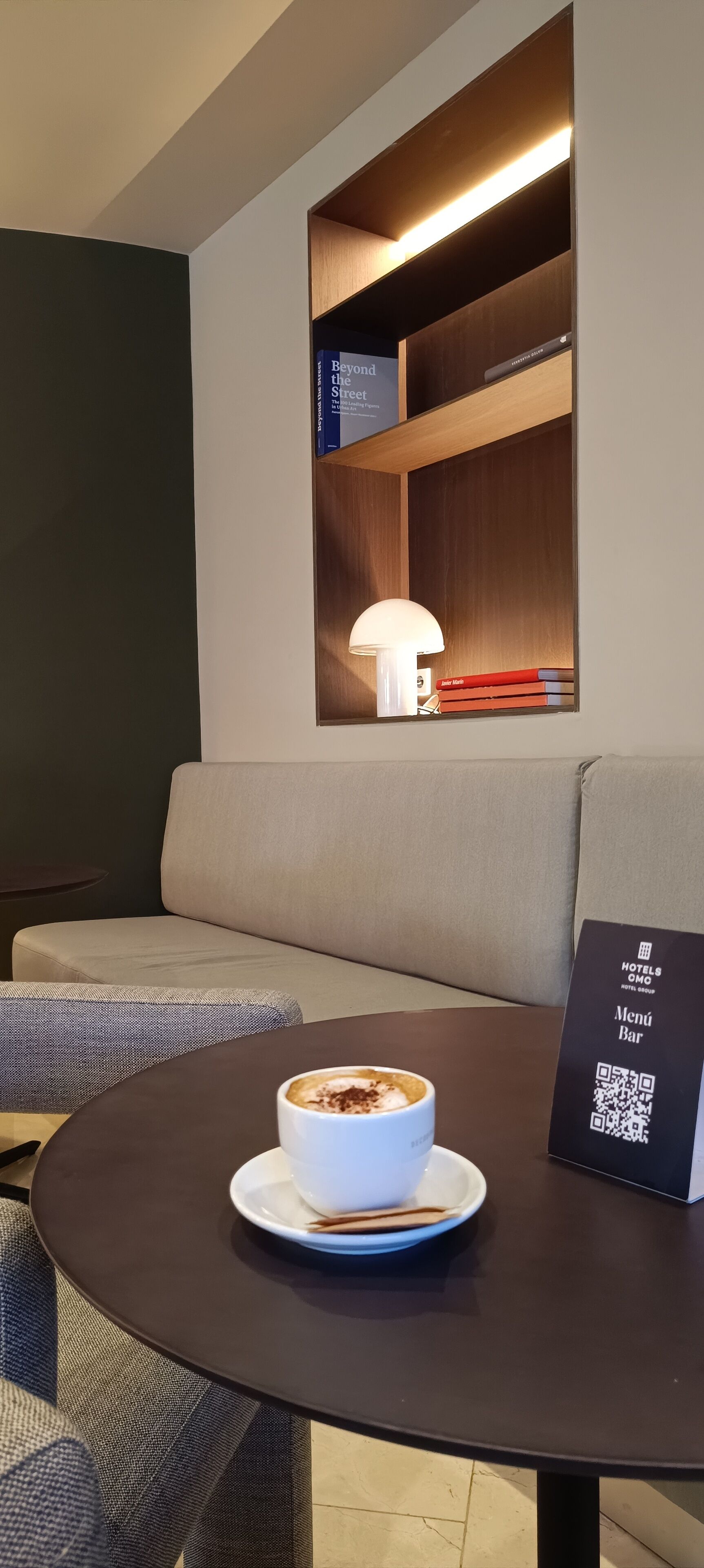 A cozy seating area with a round table, a cup of coffee, and a QR code for the hotel bar.