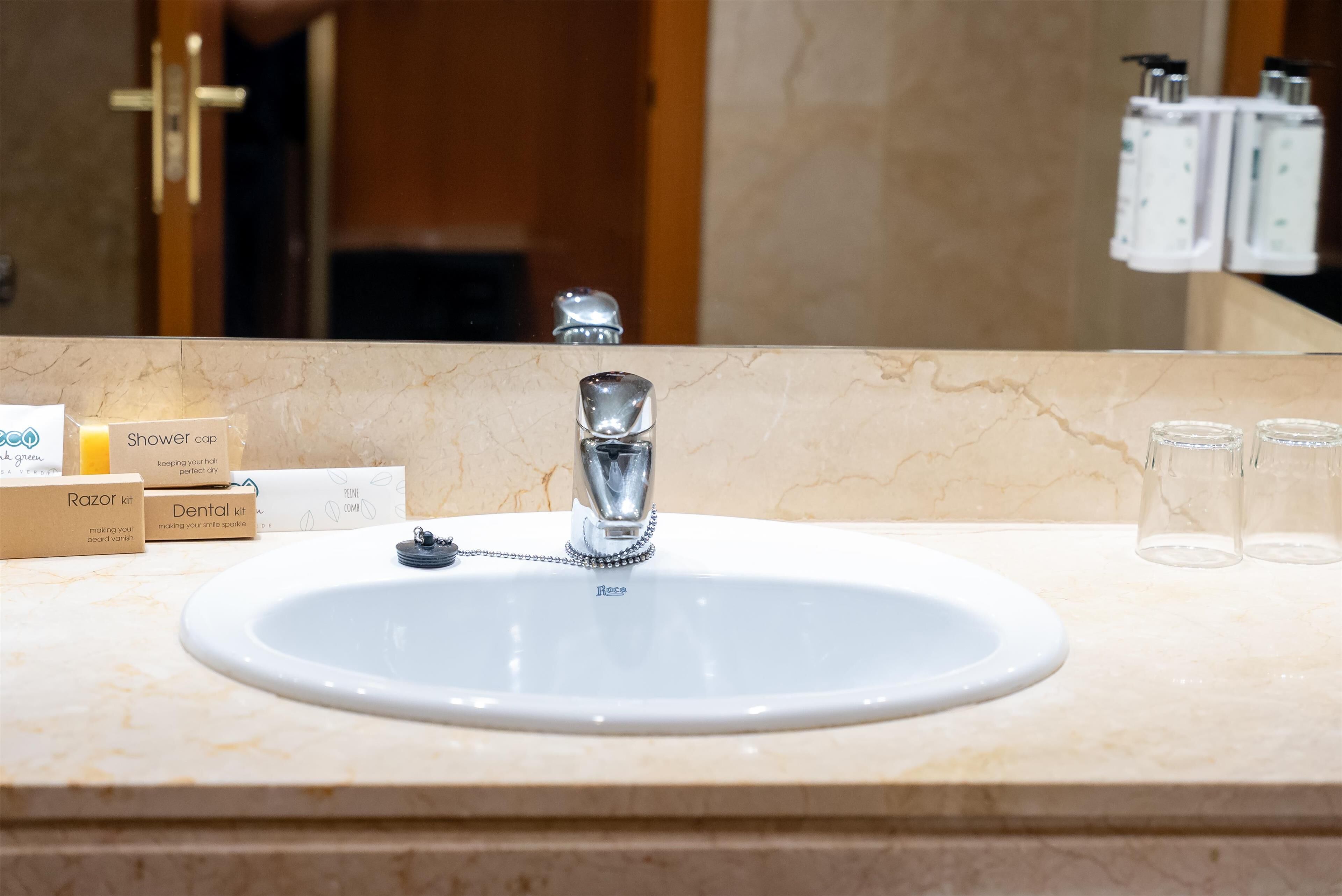 A bathroom sink with a mirror, a shower cap, a razor kit, a dental kit, and two empty glasses on the counter.