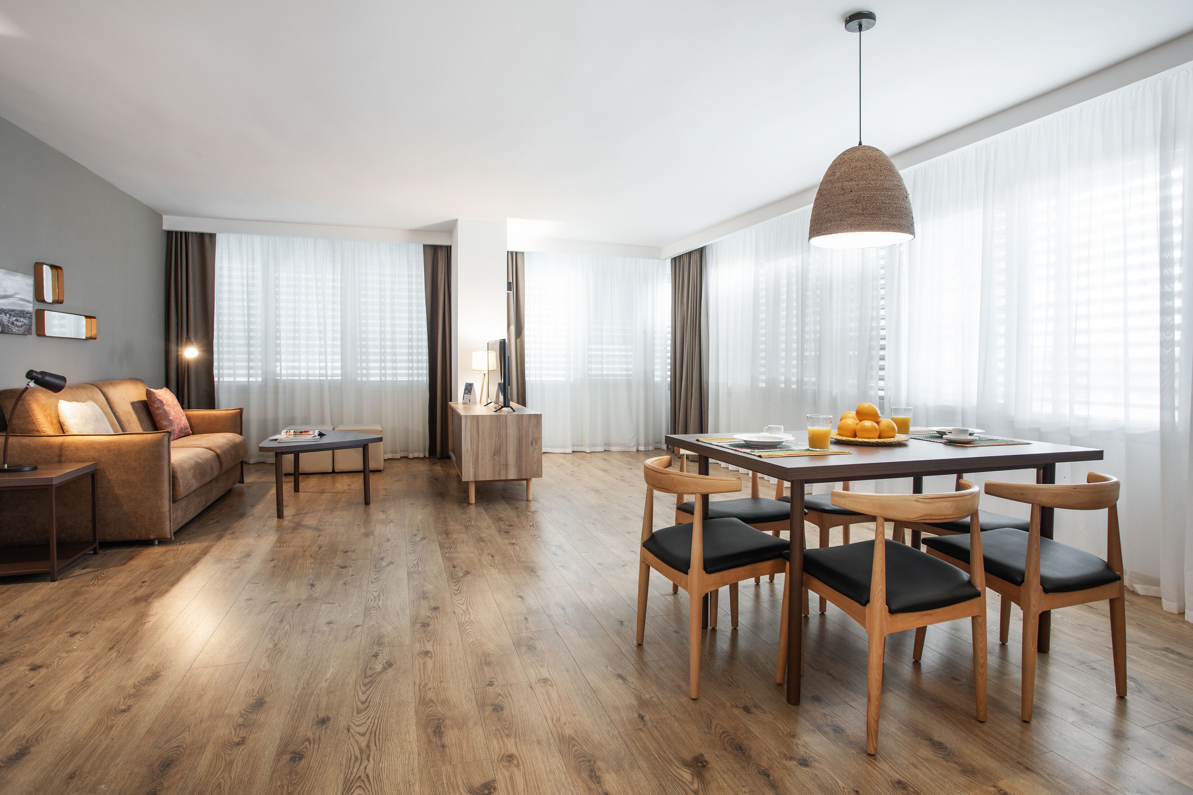 A modern living room with a wooden floor, a sofa, a coffee table, and a dining area with wooden chairs and a table.