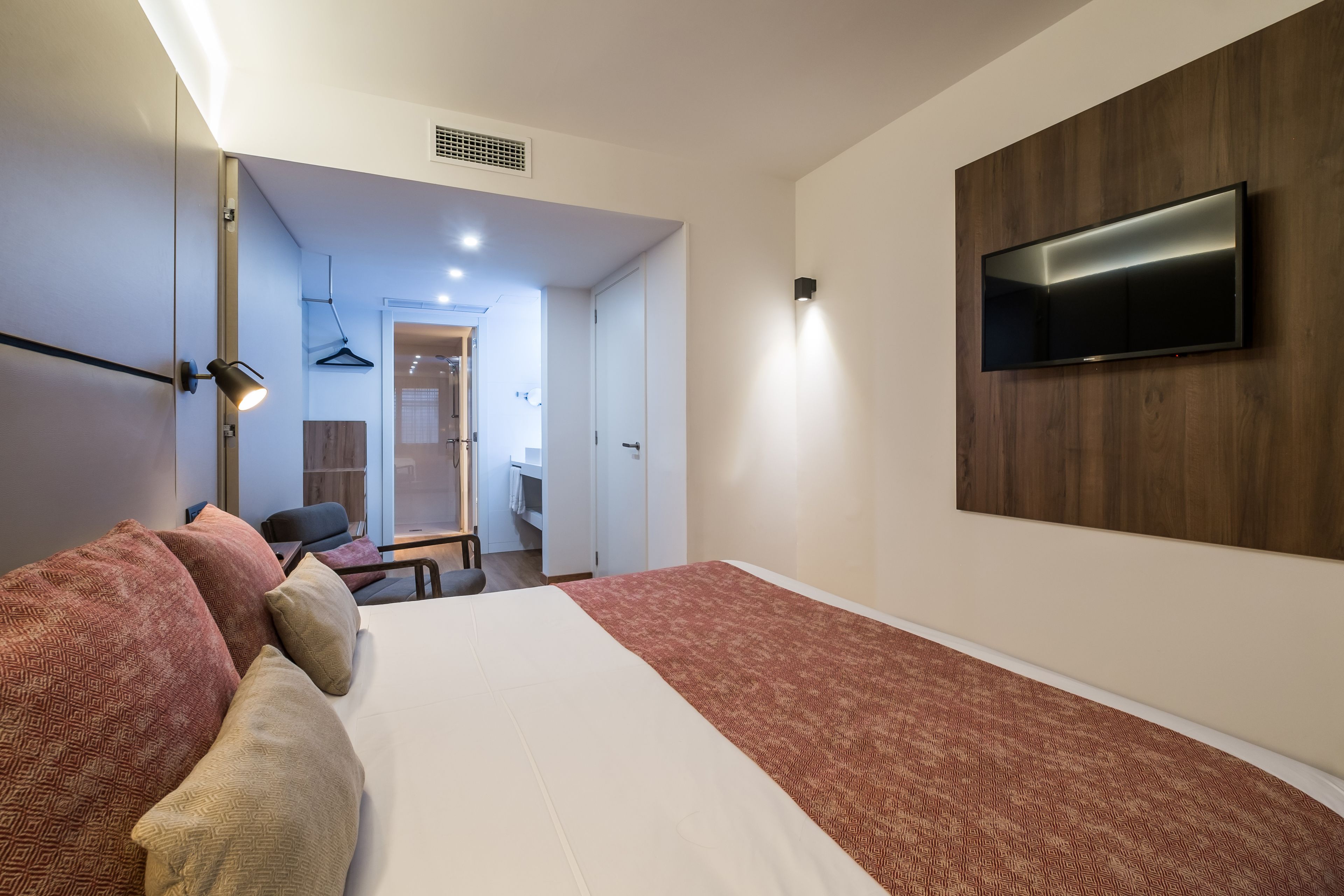 Un dormitorio moderno con una cama grande, televisor montado y vestidor.