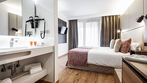 A modern hotel room with a large bed, a vanity with a mirror, a hairdryer, and a television mounted on the wall. - Pierre & Vacances Apartamentos Edificio Eurobuilding 2 (Madrid)