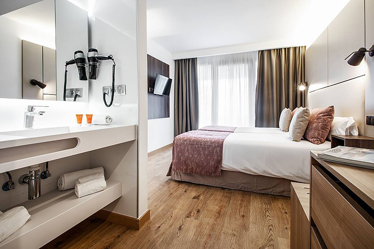 Quarto de hotel moderno com uma cama grande, uma toucador com espelho, um secador de cabelo e uma televisão na parede.