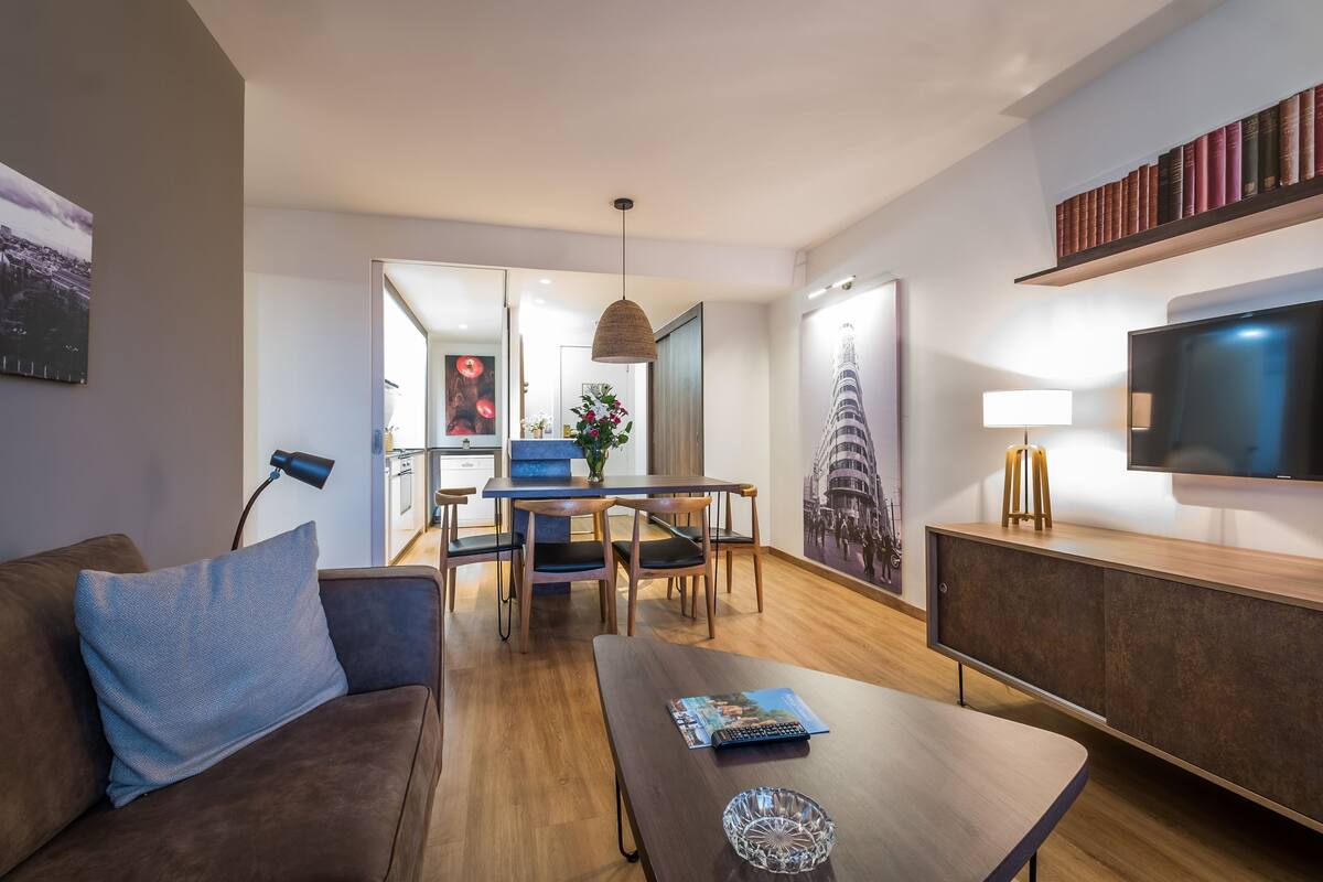 Uma sala de estar moderna com sofá, mesa de centro, televisão e uma área de jantar com cadeiras e mesa.