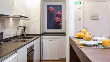 Una cocina moderna con lavavajillas, pileta y un cuadro colgado en la pared con manzanas.
