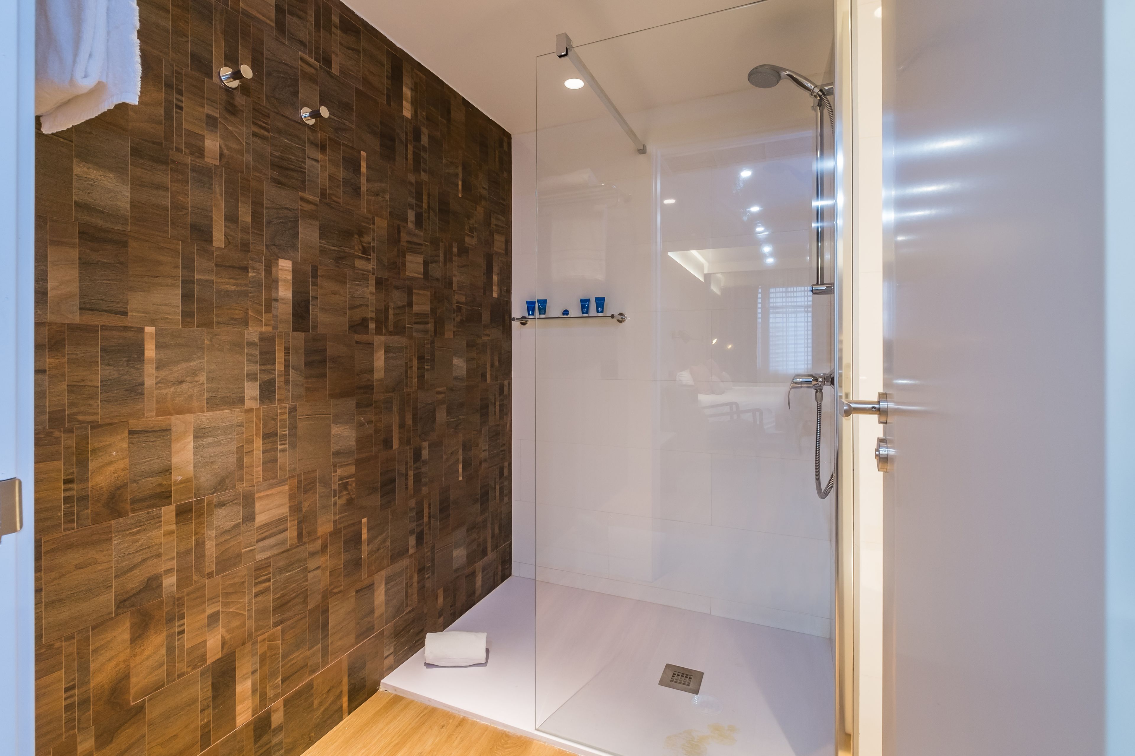 Un baño moderno con pared de madera, cabina de ducha de vidrio y lavamanos blanco.