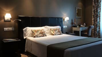 Un cuarto de hotel con una cama grande, dos almohadones decorativos, lámparas de noche, un escritorio con una silla y un espejo en la pared.