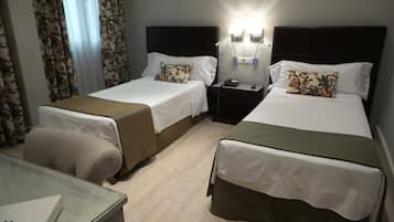 A hotel room with two beds, a desk, and a nightstand with a lamp.