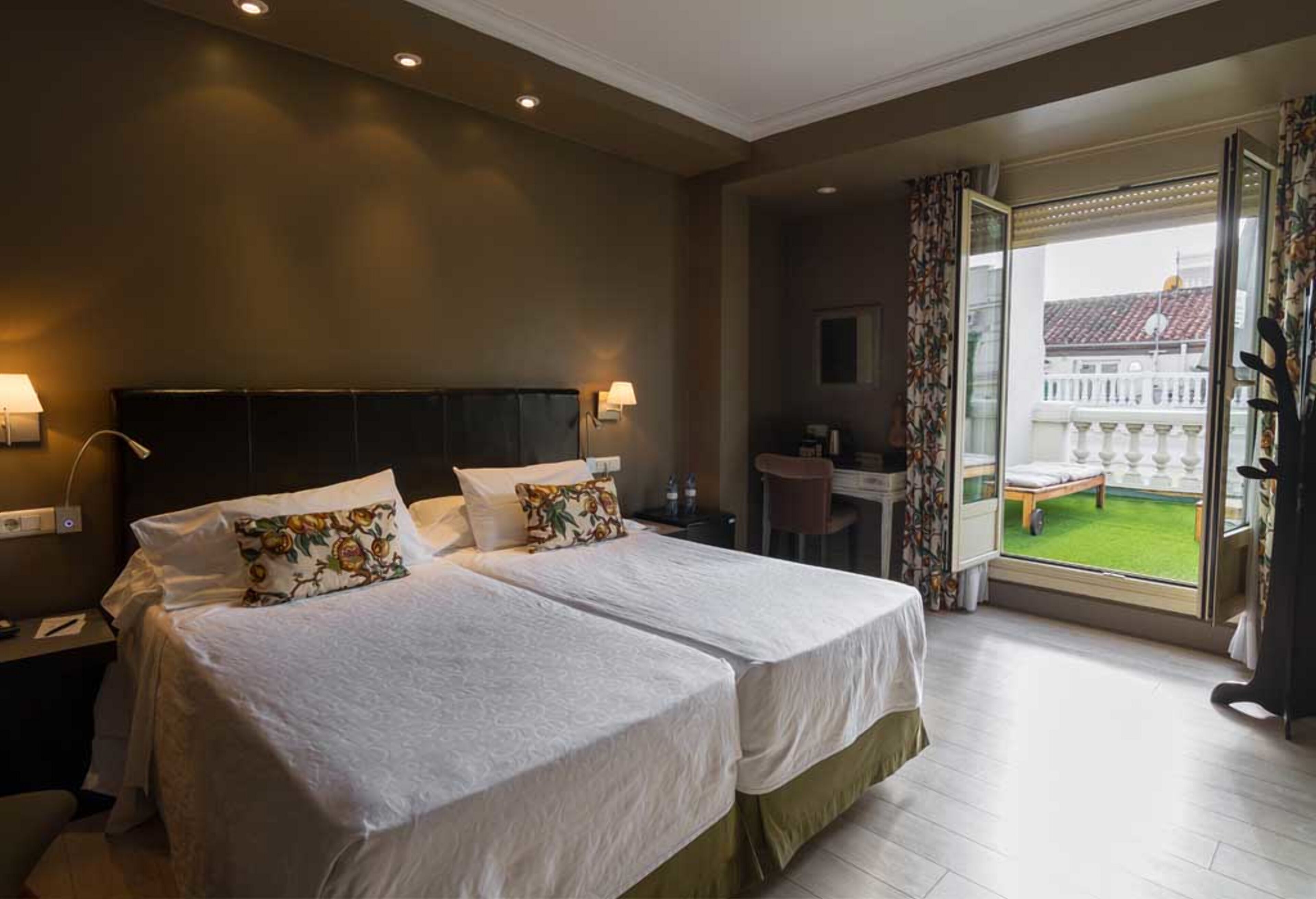 Habitación de hotel con dos camas, un escritorio y un balcón con vistas.