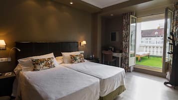 Habitación de hotel con dos camas, un escritorio y un balcón con vistas.