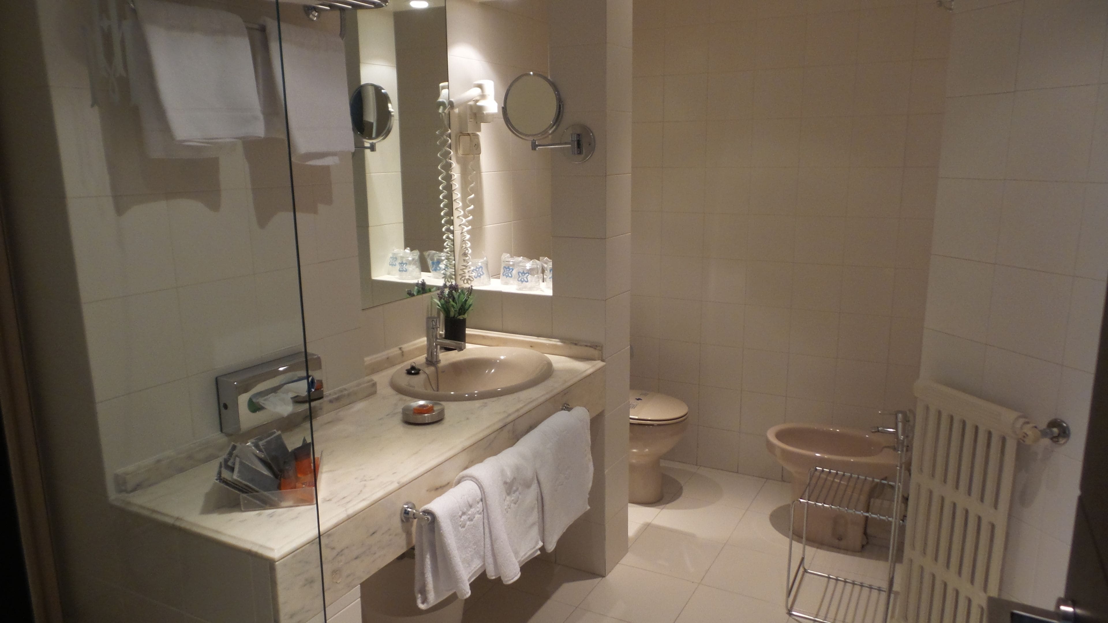 Een moderne badkamer met een douchecabine van glas, een wastafel met spiegel, een toilet en een radiator.