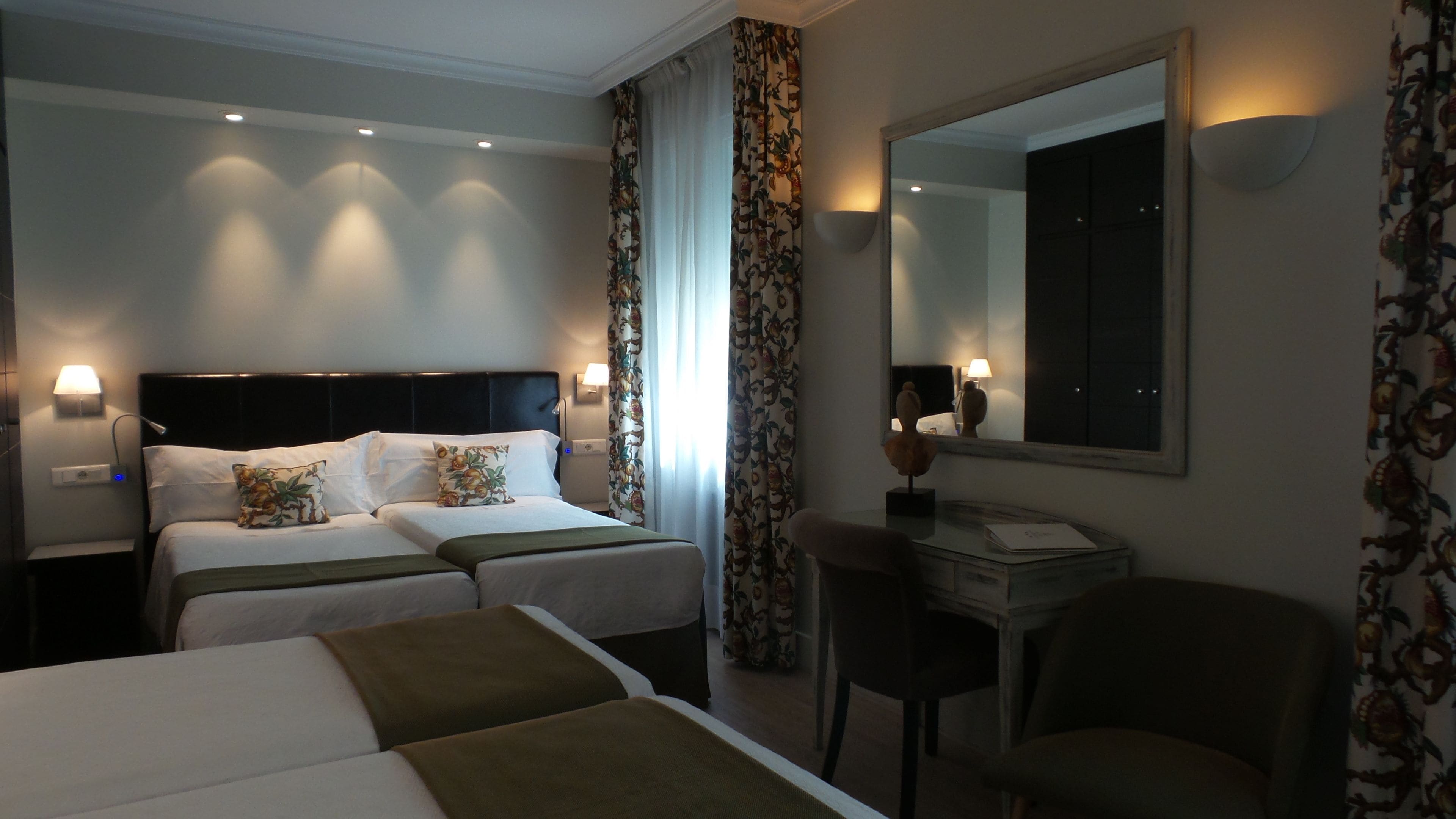 Habitación de hotel con dos camas, un escritorio, una silla y un espejo grande.