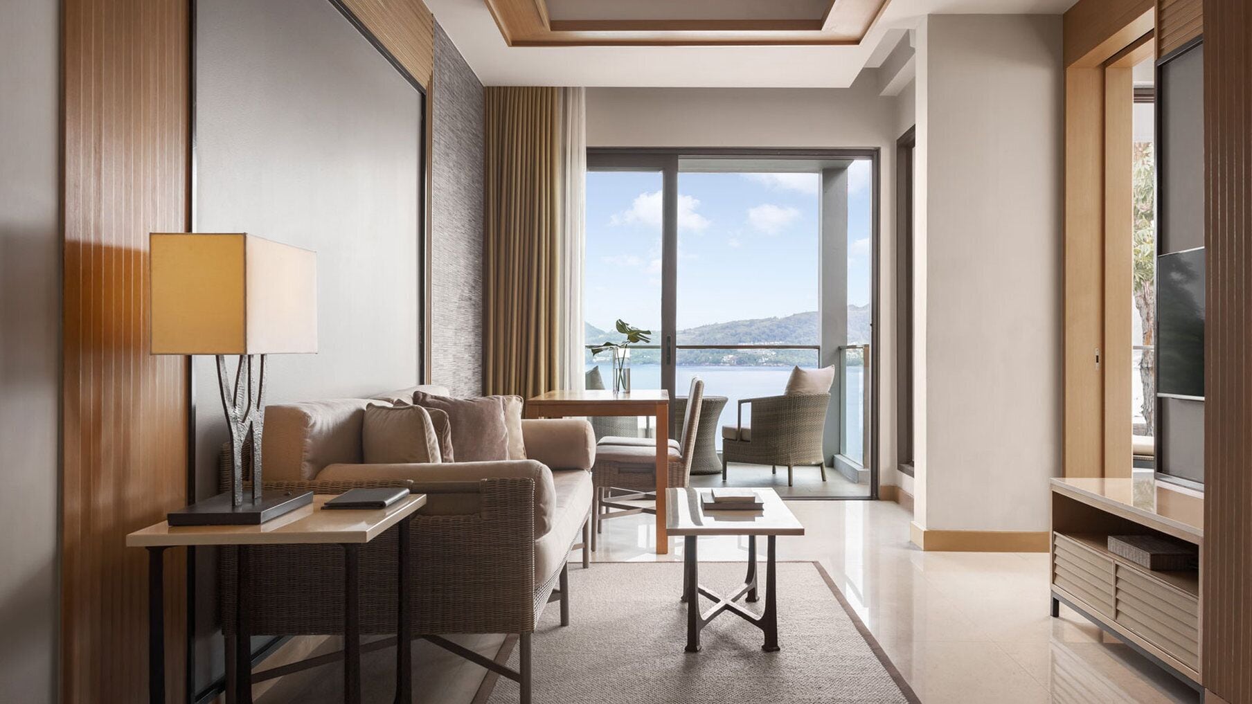 A modern hotel room with a balcony, a sofa, a table, and a TV.