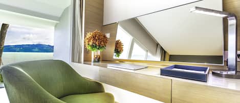 A modern room with a green chair, a desk with a laptop, a mirror, and a view of the outdoors.