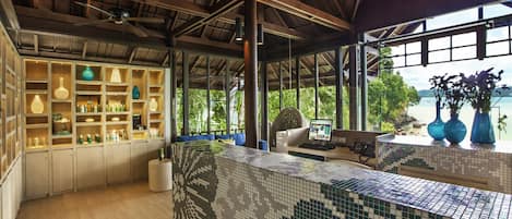 Amplia habitación con salpicadero de azulejos, estantes de madera con diversos objetos, una silla colgante y vista al mar a través de amplias ventanas.