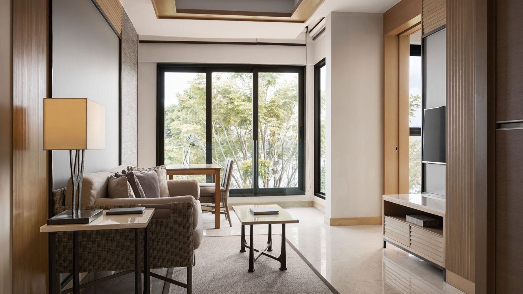 A modern living room with a sofa, a small table, a lamp, and a large window offering a view of trees.