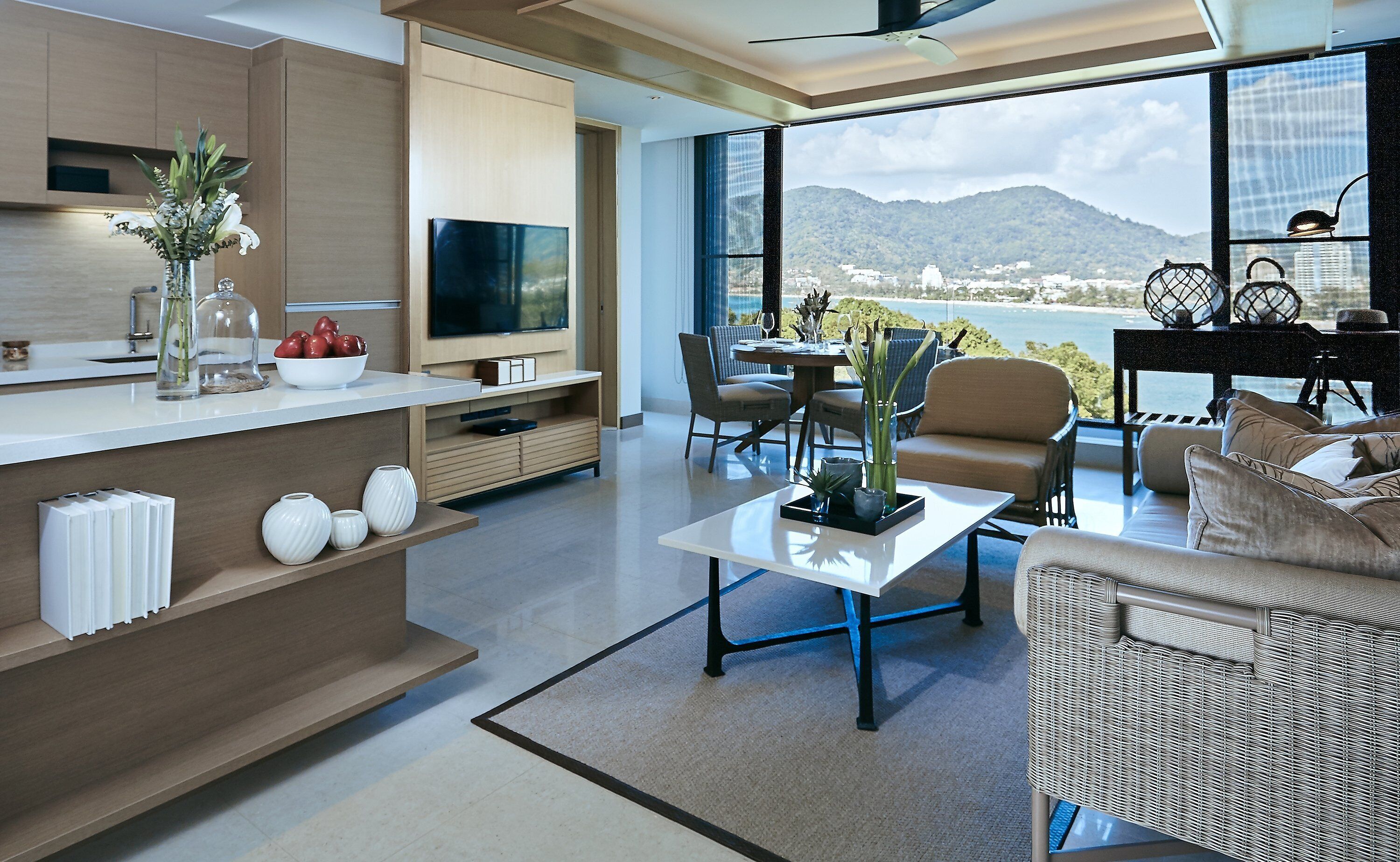 A modern living room with a large TV, dining area, and a view of the mountains.