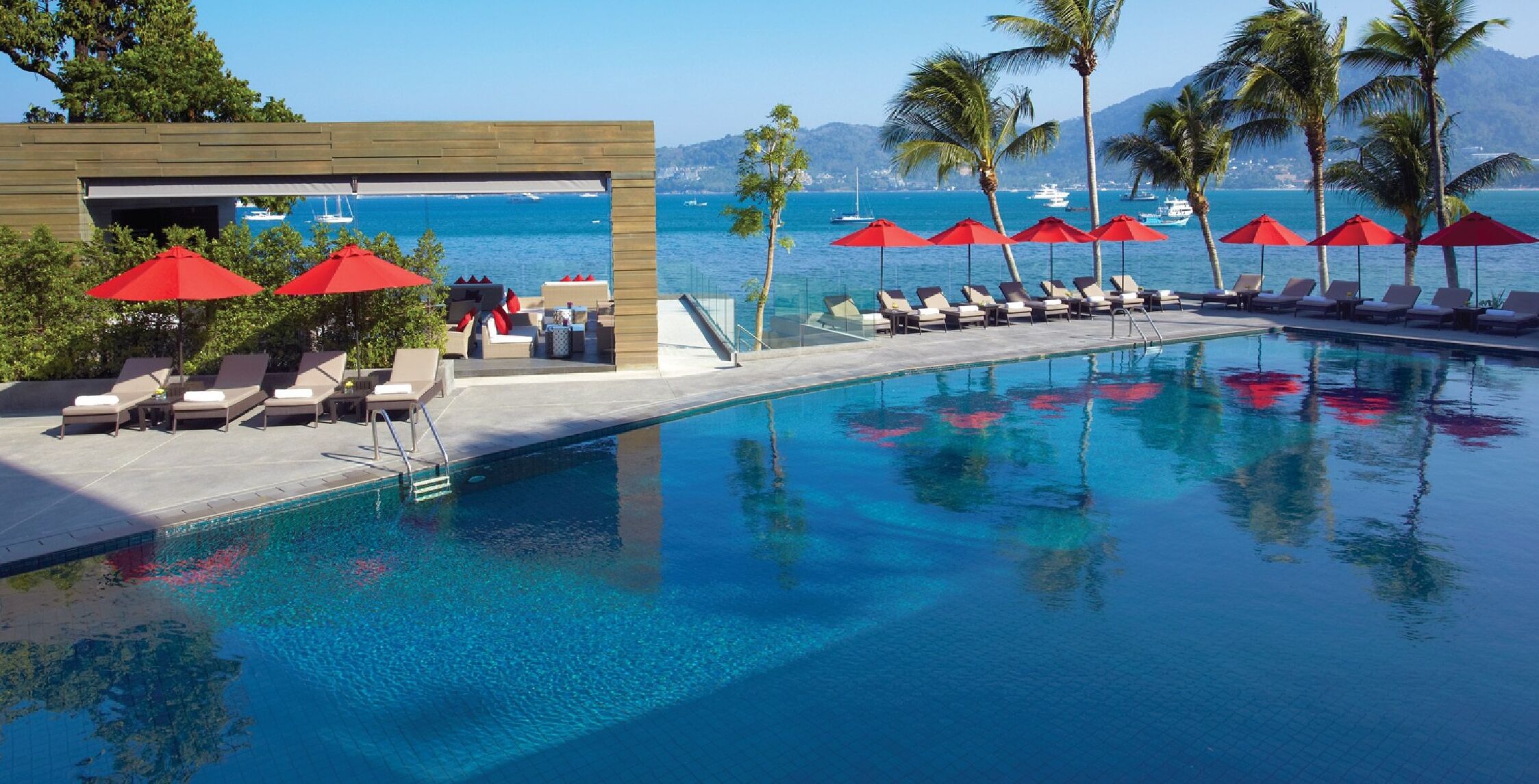 Un espace piscine avec des chaises longues et des parasols, une structure en bois et une vue sur la mer.