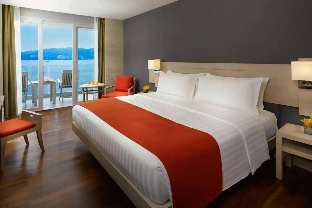 Hotelkamer met een groot bed, een bureau met stoel, een televisie en een balkon met uitzicht op het water.