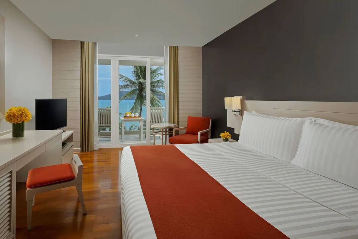 Een hotelkamer met een bed, een bureau, een stoel, een televisie en uitzicht op de oceaan.