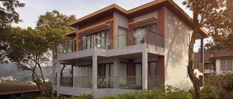 A modern two-story house with large glass windows and balconies, surrounded by lush greenery.