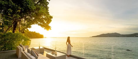 A serene outdoor seating area with a view of the sea at sunset.