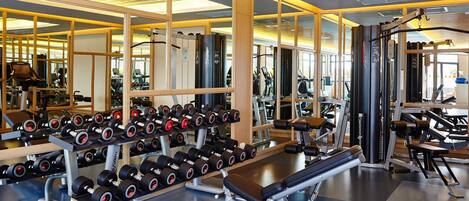 Un gimnasio con equipo de levantamiento de pesas, máquinas de ejercicio y espejos.