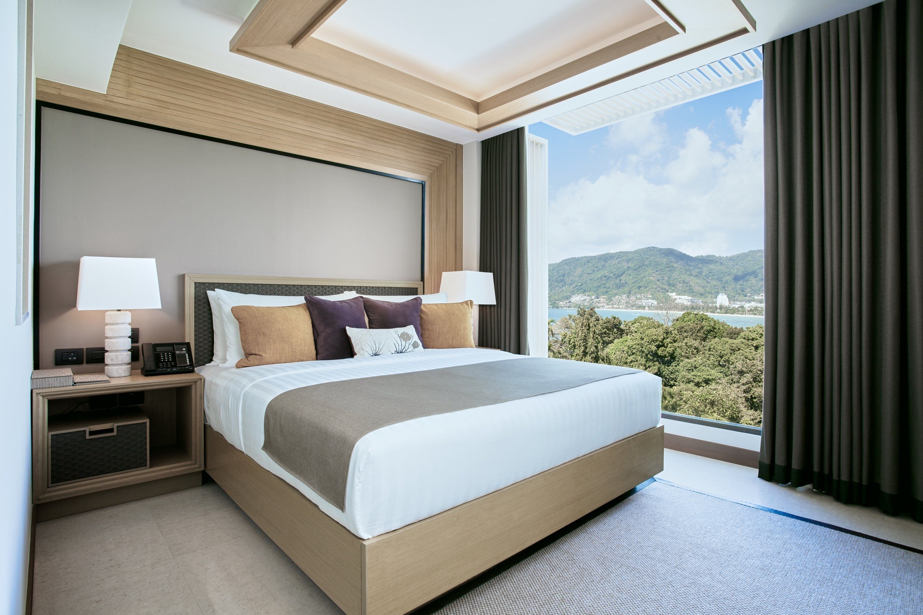Een hotelkamer met een groot bed, bedlampen, een telefoon en uitzicht op een stad en bergen.