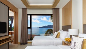 Habitación de hotel con dos camas, televisión, escritorio y vista al mar.