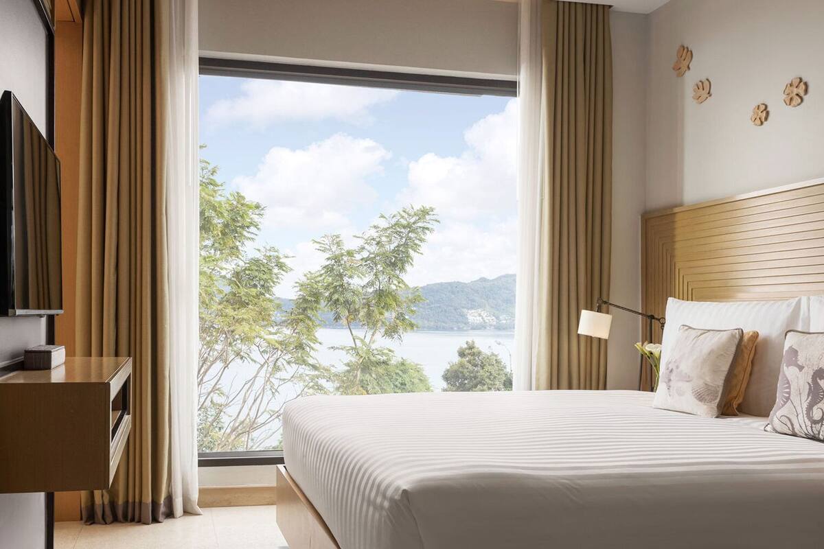 Een hotelkamer met een groot bed, een televisie, een bureau en uitzicht op een meer en bergen.