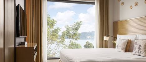 Habitación de hotel con una cama grande, televisión, escritorio y vistas a un lago y montañas.