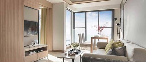 A modern living room with a sofa, coffee table, and a TV. There is a balcony with a table and chairs.