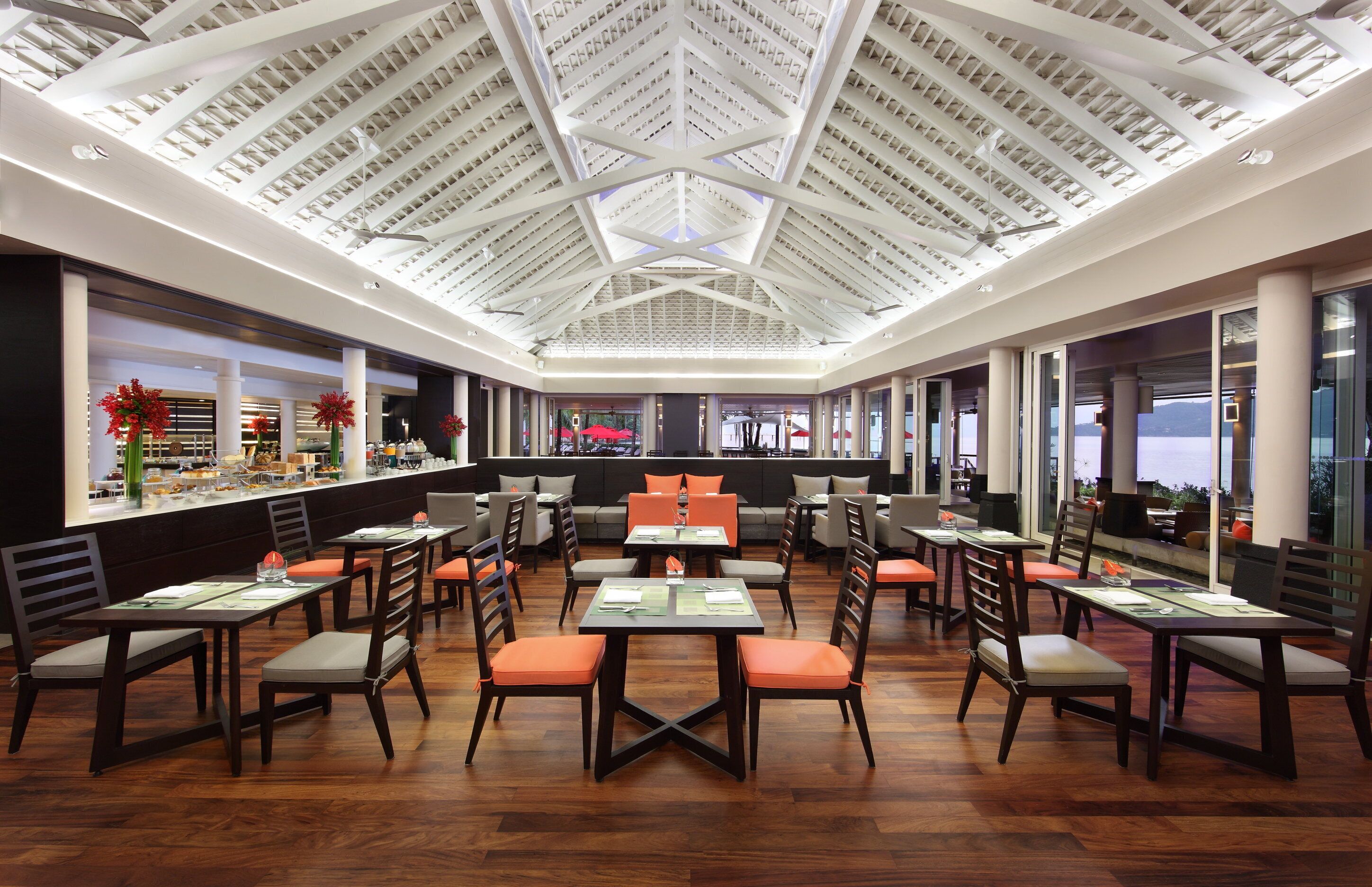 Een ruim restaurant met een hoge plafond en natuurlijk licht, met tafels en stoelen klaar voor het dineren.