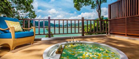 A hot tub surrounded by a wooden deck, overlooking a body of water and mountains.