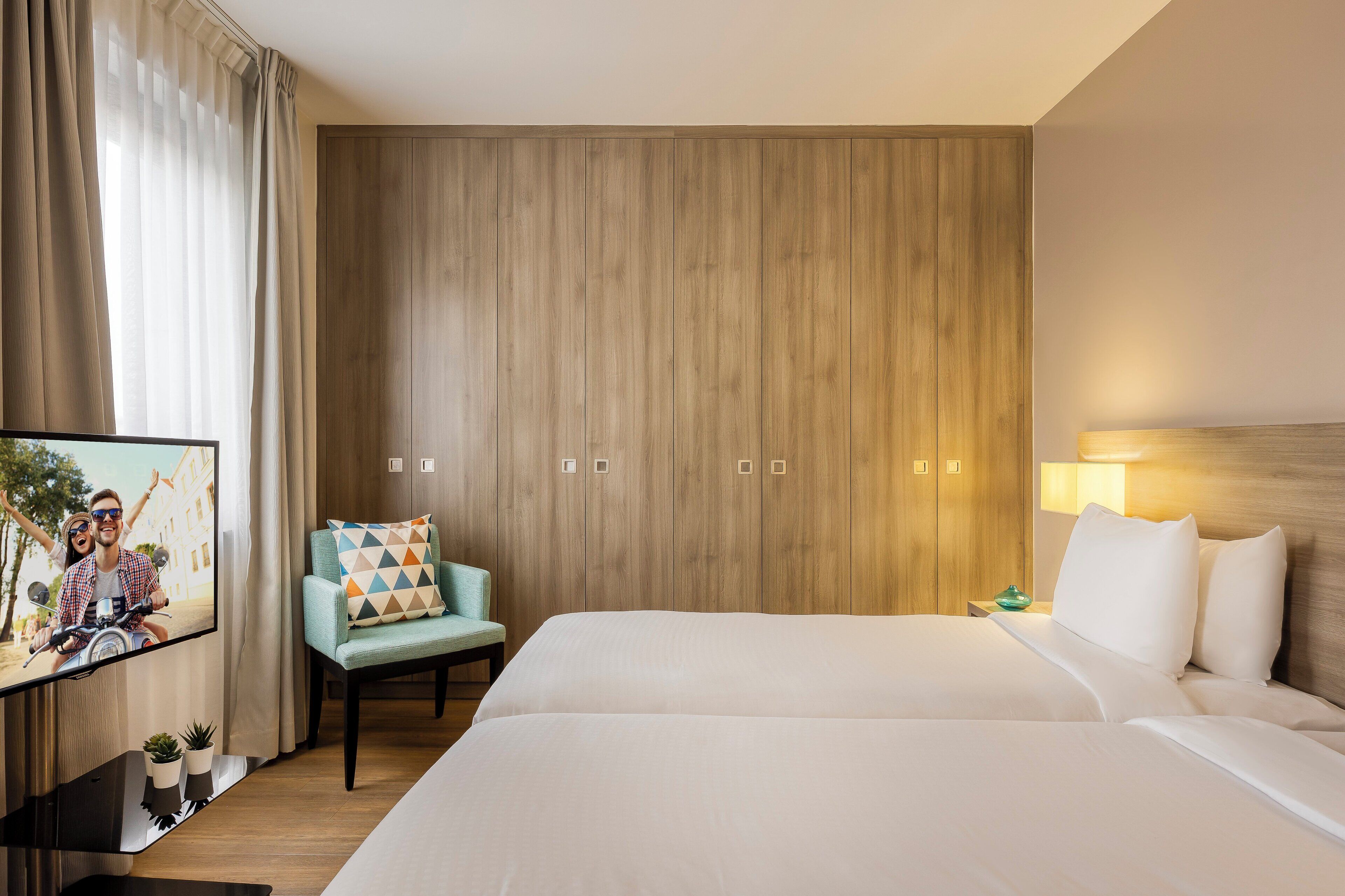 Een hotelkamer met een groot bed, een televisie op een standaard, een stoel en een houten wandpaneel.