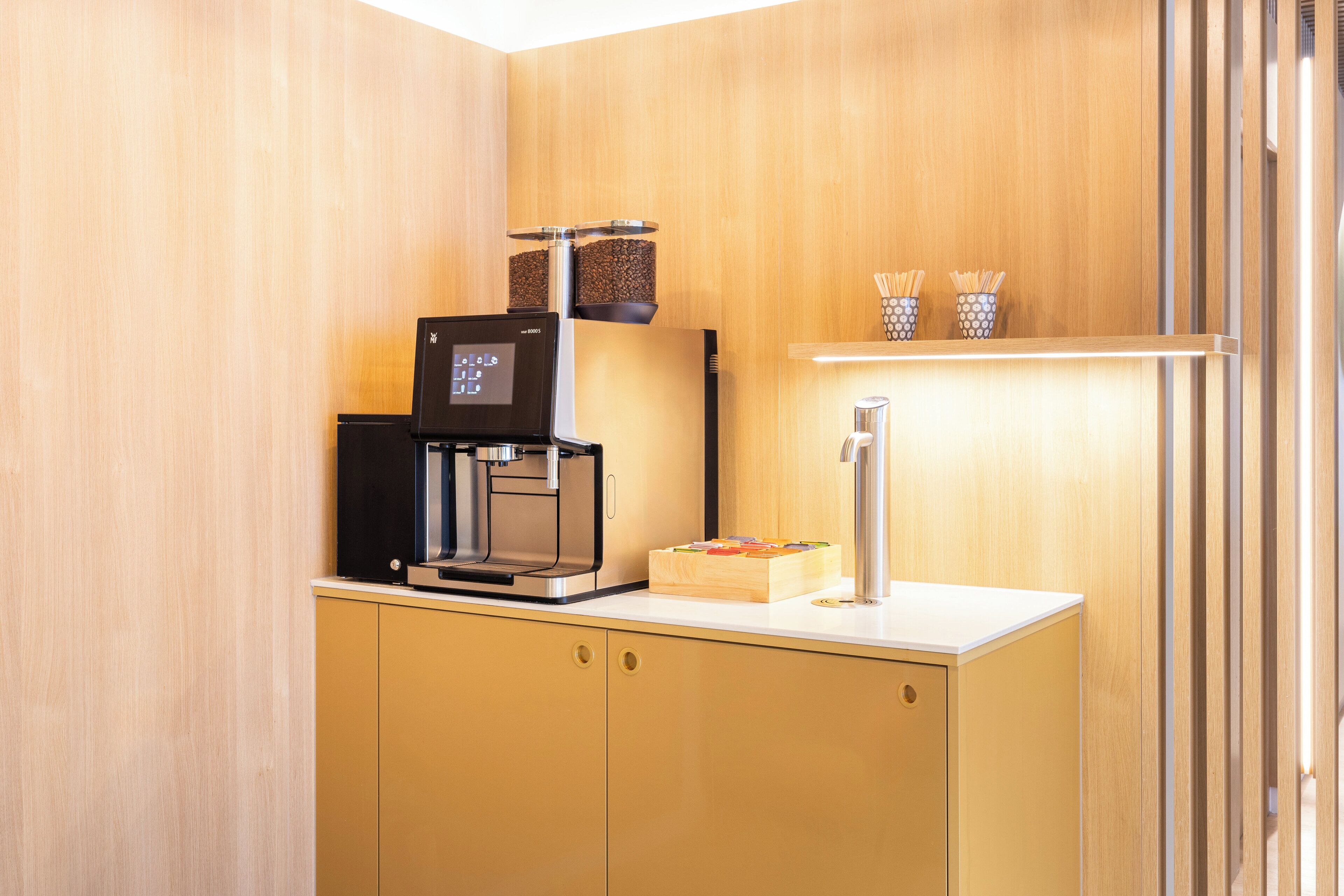 Une petite cuisine équipée d’une machine à café, d’un petit réfrigérateur et d’un meuble en bois.