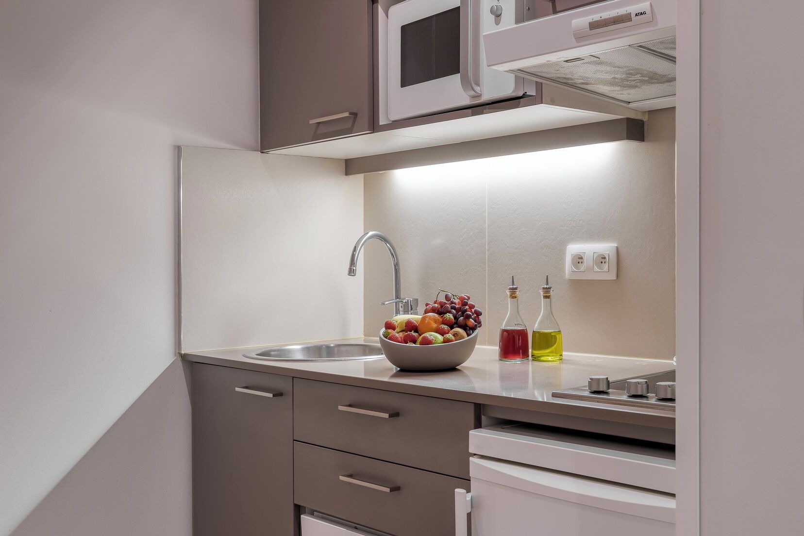 A compact kitchen with a built-in microwave, a stainless steel sink, and a bowl of fruit on the counter.