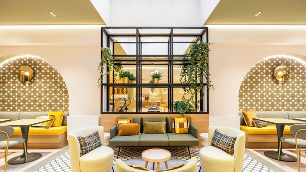 A modern lobby with a central seating area, a glass partition with plants, and a patterned floor. - Citadines Toison d'Or Brussels (Brussels)