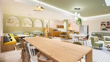 A modern dining area with a long wooden table, multiple chairs, and a seating area with cushions.