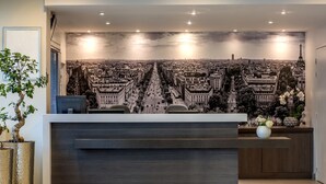 A reception desk with a cityscape mural, a potted plant, and a vase of flowers. - Citadines Montparnasse Paris (Paris)